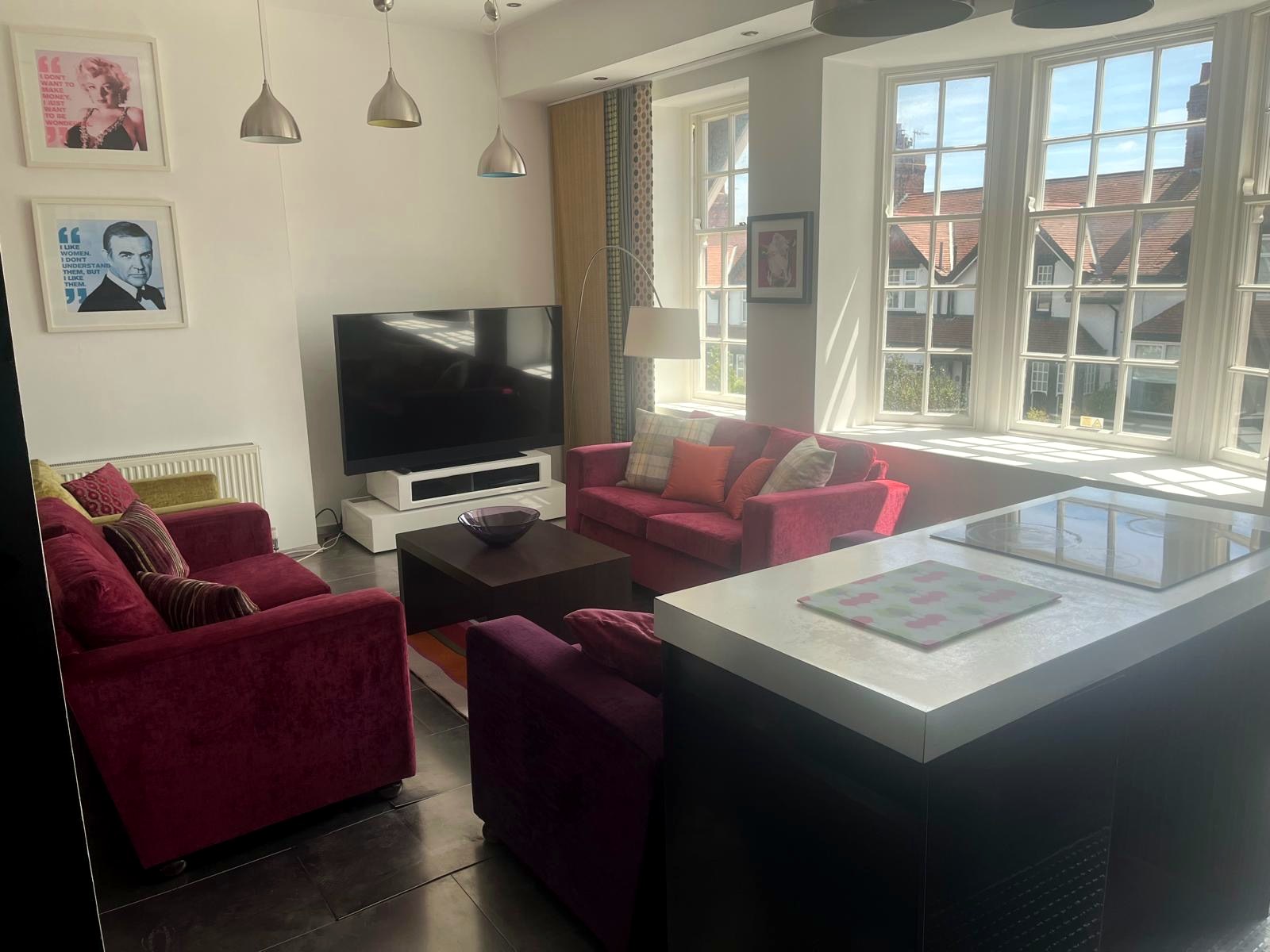 Bright open-plan living room with red sofas, large TV and big windows